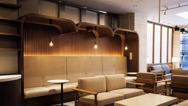 Un área de estar moderna con un sofá, mesas y una pared de madera decorativa con iluminación empotrada.