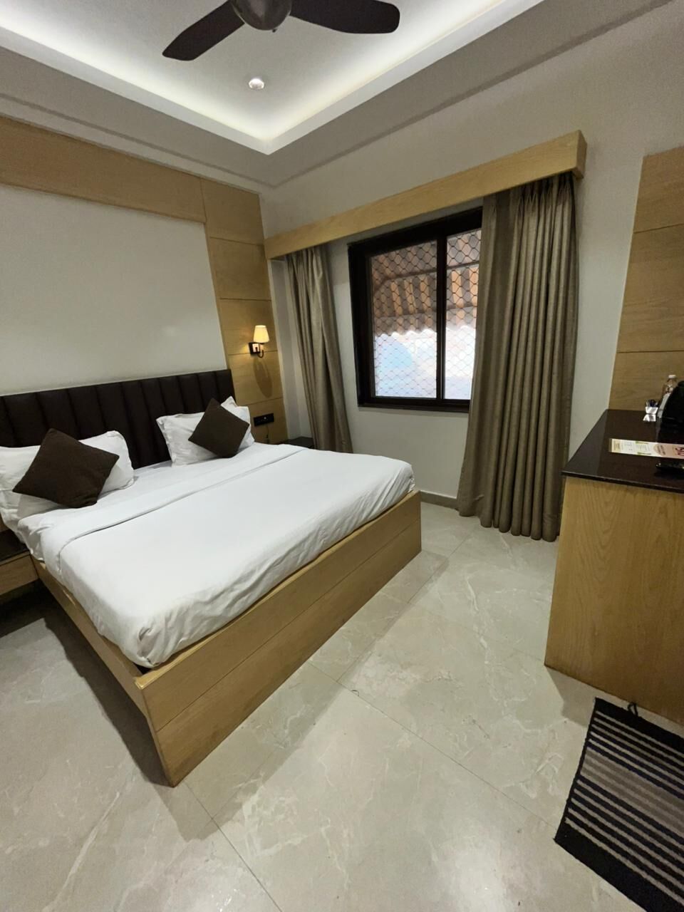 Een hotelkamer met een bed, een bureau, een raam met gordijnen en een plafondventilator.
