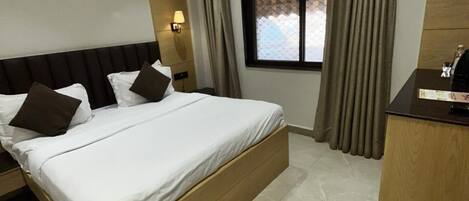 Een hotelkamer met een bed, een bureau, een raam met gordijnen en een plafondventilator.