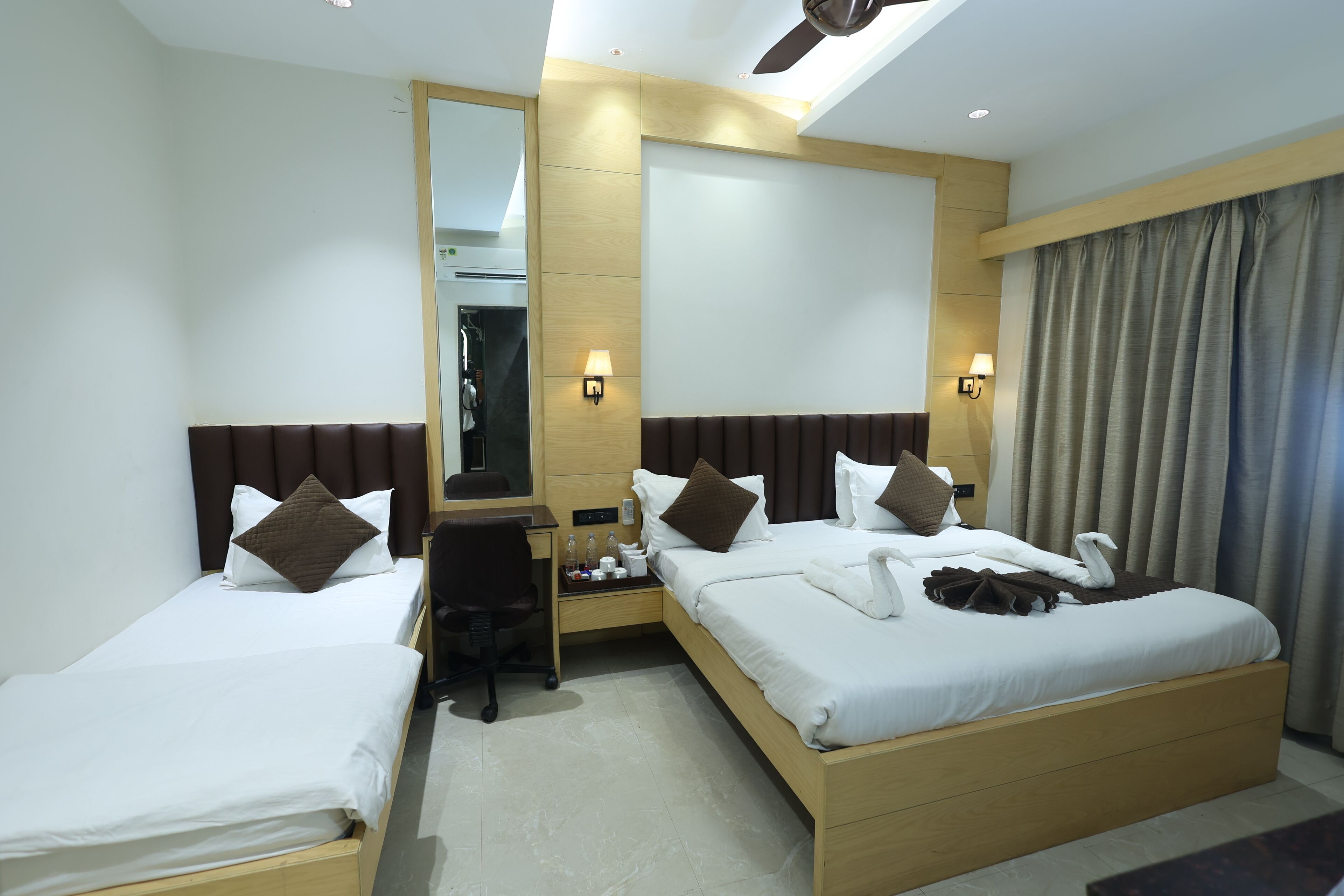 A hotel room with two beds, a desk, a chair, a mirror, and a window with curtains.