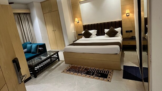 A modern hotel room with a large bed, a sofa, a ceiling fan, and a large mirror. - Hotel sar kamla dham (Mathura)
