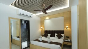 A modern hotel room with a large bed, a ceiling fan, a mirror, and a nightstand with a lamp. - Hotel sar kamla dham (Mathura)