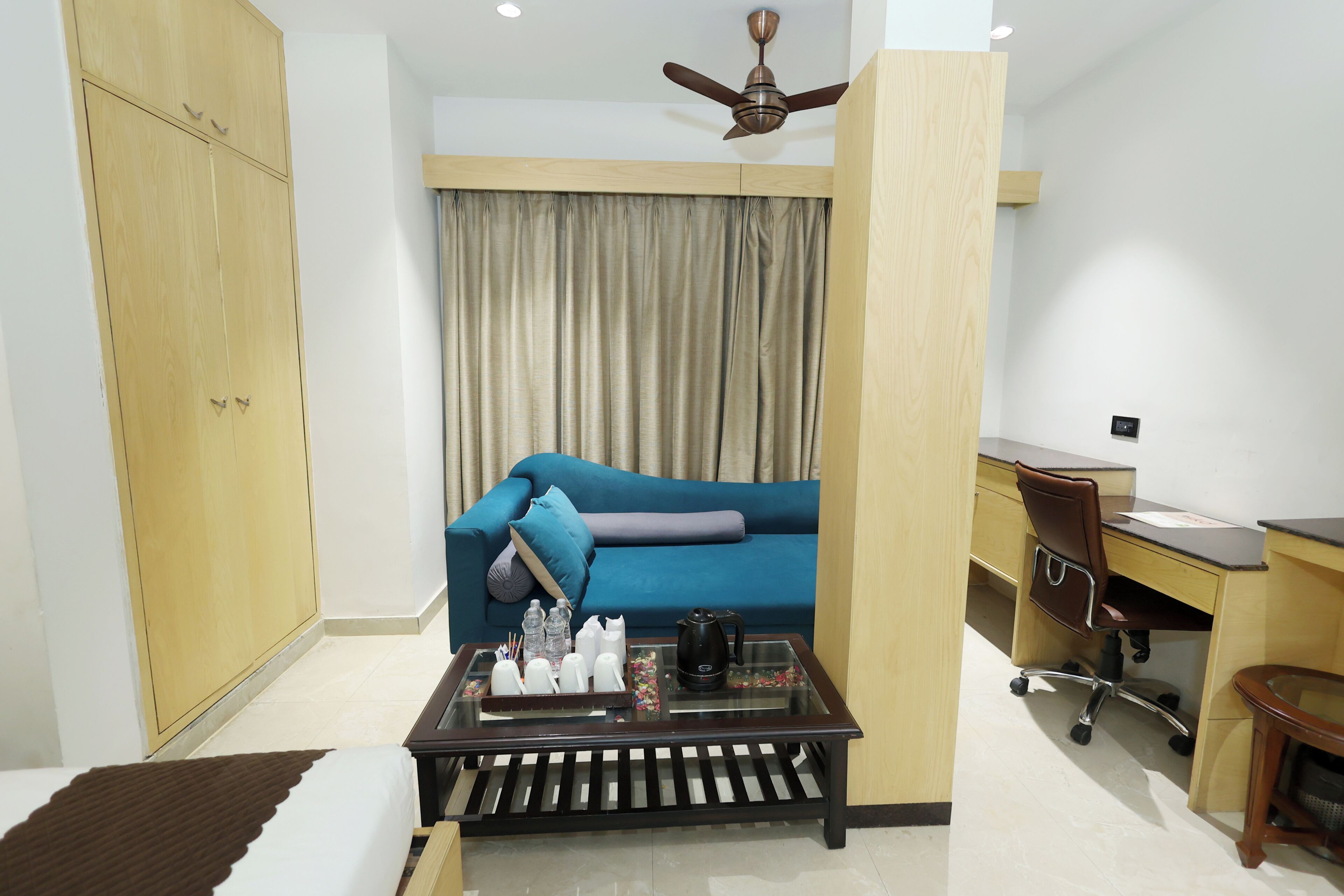 Habitación de hotel con cama, escritorio, silla, sofá, mesa de centro y ventilador de techo.