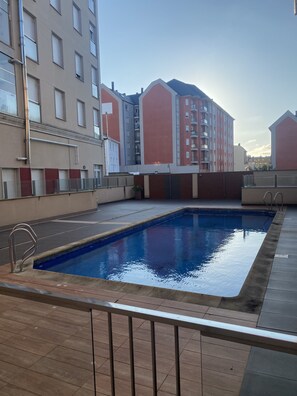 A swimming pool with a tiled deck, surrounded by buildings with balconies and a clear sky. - LUXURY DUPLEX IN FOZ WITH SEA VIEWS (Foz)
