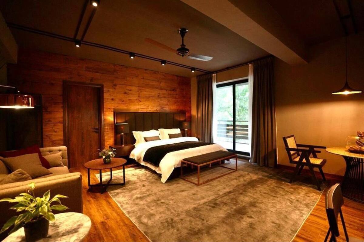 Quarto moderno com uma cama grande, uma parede de destaque em madeira, uma área de refeições e vista para o exterior.