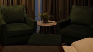 A room with two green armchairs, a small round table with a plant, and a large window with curtains. - Byarsa Hotel Skardu (Skardu)