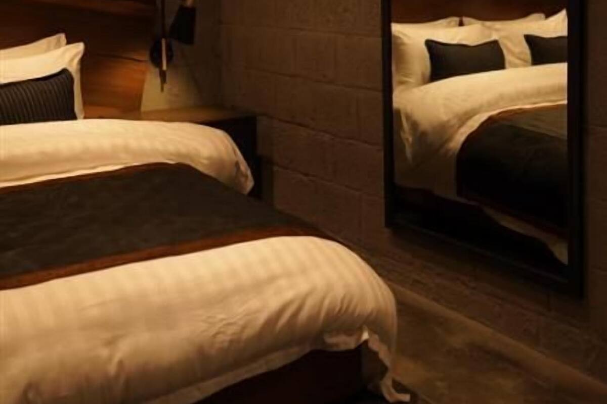 Quarto de hotel com parede de tijolos, cabeceira de madeira, uma cama de solteiro com roupa de cama branca e um espelho grande na parede.