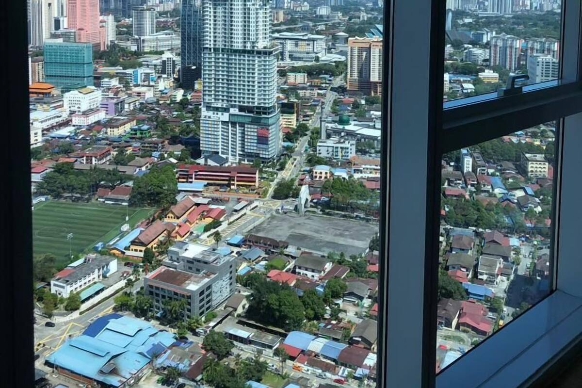 A cityscape viewed from a high-rise window, featuring a mix of residential and commercial buildings, a prominent high-rise hotel, and a distant mountain range.