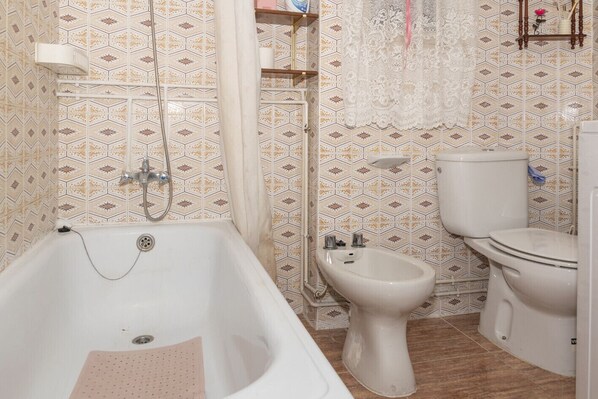 Een badkamer met een bad, een toilet en een hygiëneschuimer.