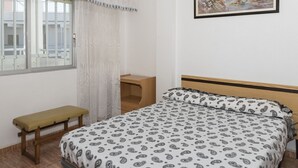 Una camera da letto con un letto, una panca, un comodino in legno, una finestra con tende e un quadro appeso alla parete.