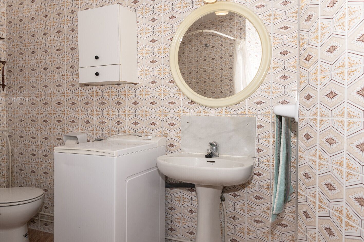 A bathroom with a toilet, a washing machine, a sink, and a mirror.