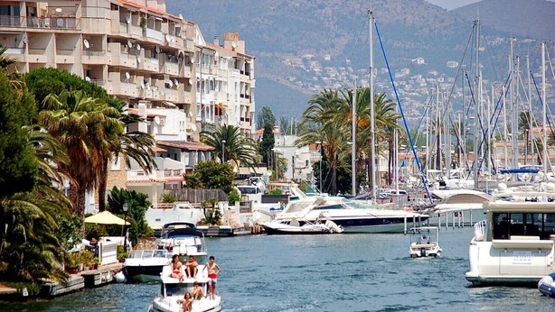 A marina with boats, a white yacht, and a building with balconies and satellite dishes.
