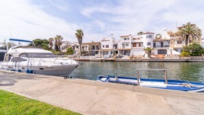 A marina with boats docked, a waterfront building with balconies, and palm trees.