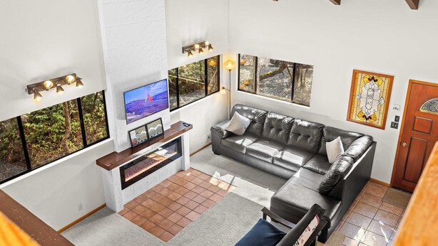 A modern living room with a leather sofa, a flat-screen TV, and large windows with a view of greenery.