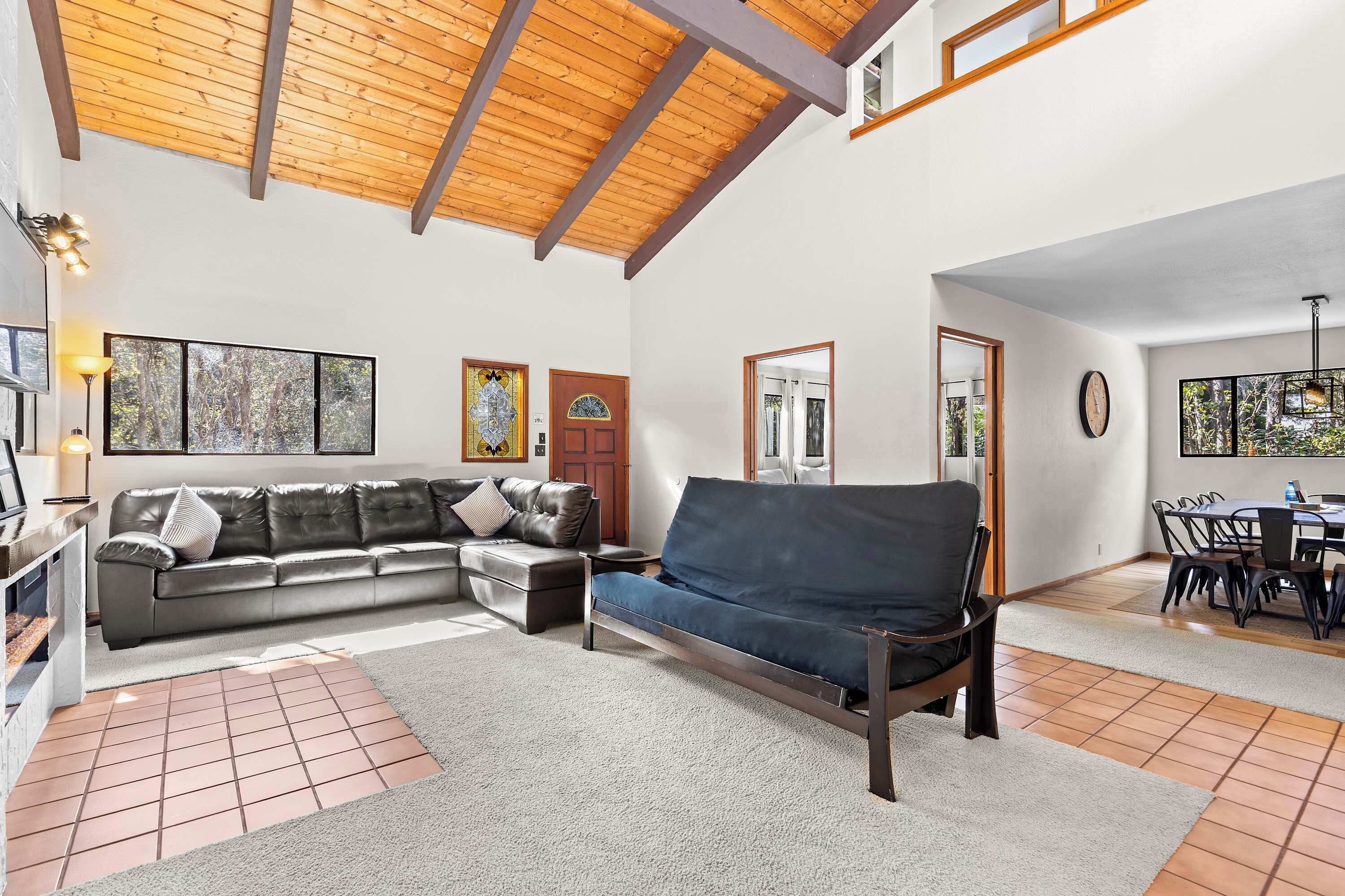 Un'ampia zona giorno con soffitto in legno, un divano componibile, un tavolo da pranzo con sedie e un'ampia finestra vista foresta.
