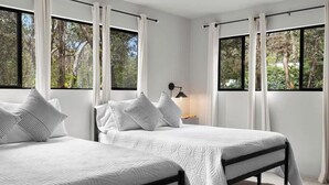 A bedroom with two beds, white bedding, and large windows with curtains.