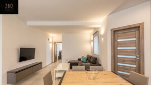Una sala moderna con televisor, una mesa de comedor de madera y un sofá.