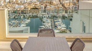 Un balcón con mesa y sillas da a un puerto deportivo con barcos y vistas de la ciudad.