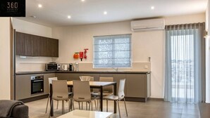 Una cocina moderna con comedor, que incluye horno empotrado, microondas y un amplio ventanal con cortinas.