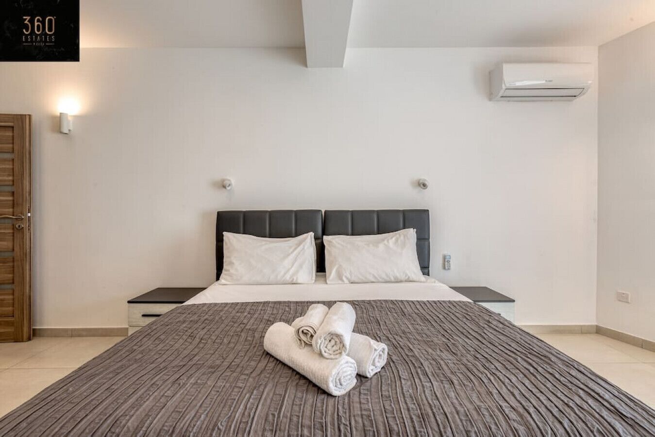 Een moderne hotelkamer met een groot bed, een hoofdeinde, een nachtkastje, een airconditioner en een bordje aan de muur.