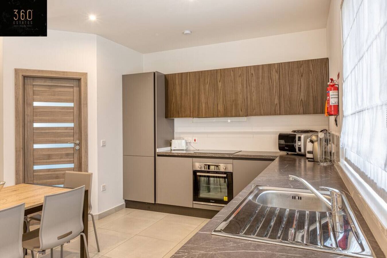 A modern kitchen with wooden cabinets, a built-in oven, a sink, and a dining area with a table and chairs.