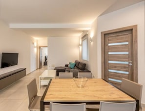 A modern living room with a TV, a wooden dining table, and a sofa.
