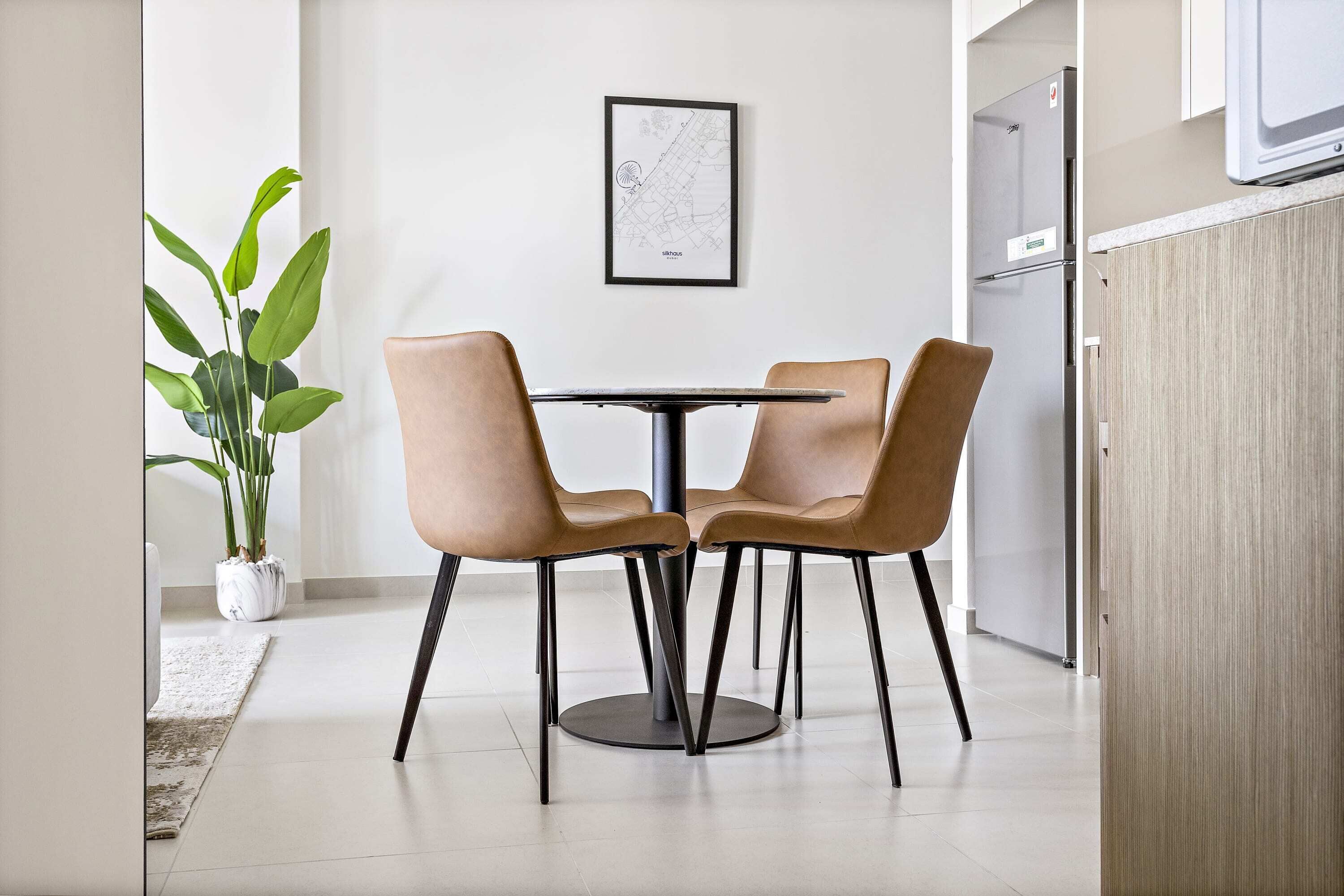 A modern dining area with a round table and four chairs, a potted plant, and a framed map on the wall.