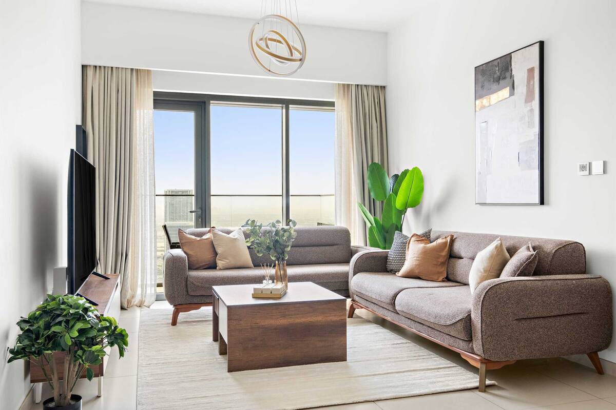A modern living room with a sofa set, a coffee table, and a large window with curtains.