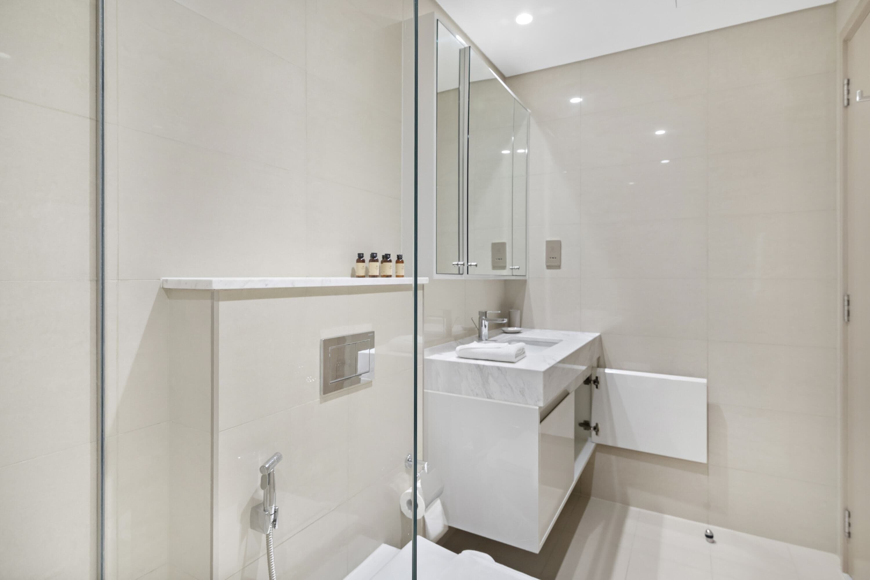 A modern bathroom with a glass shower enclosure, a white vanity with a marble countertop, and a large mirror above the sink.