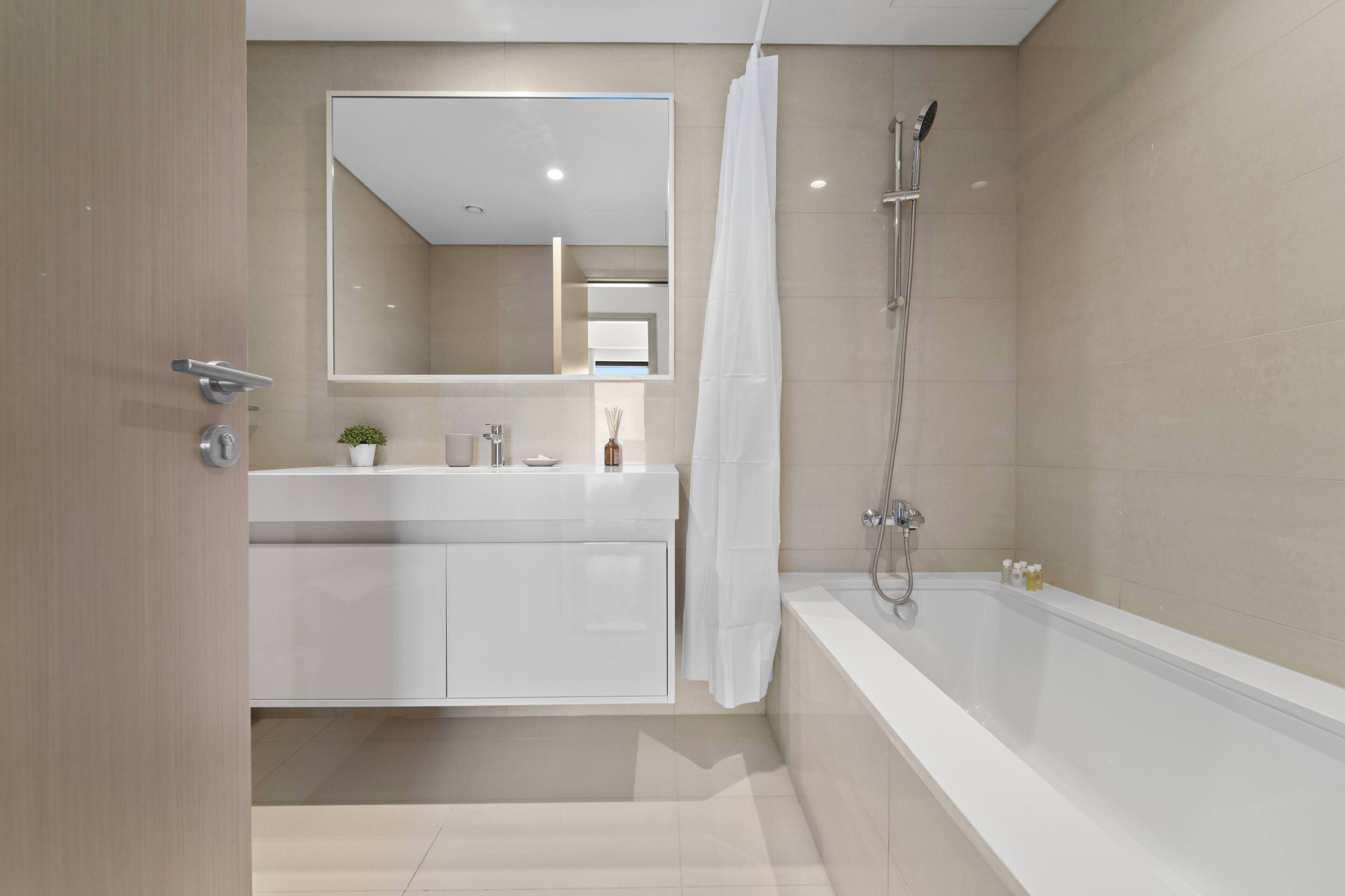A modern bathroom with a white vanity, a large mirror, a shower with a glass door, and a bathtub.