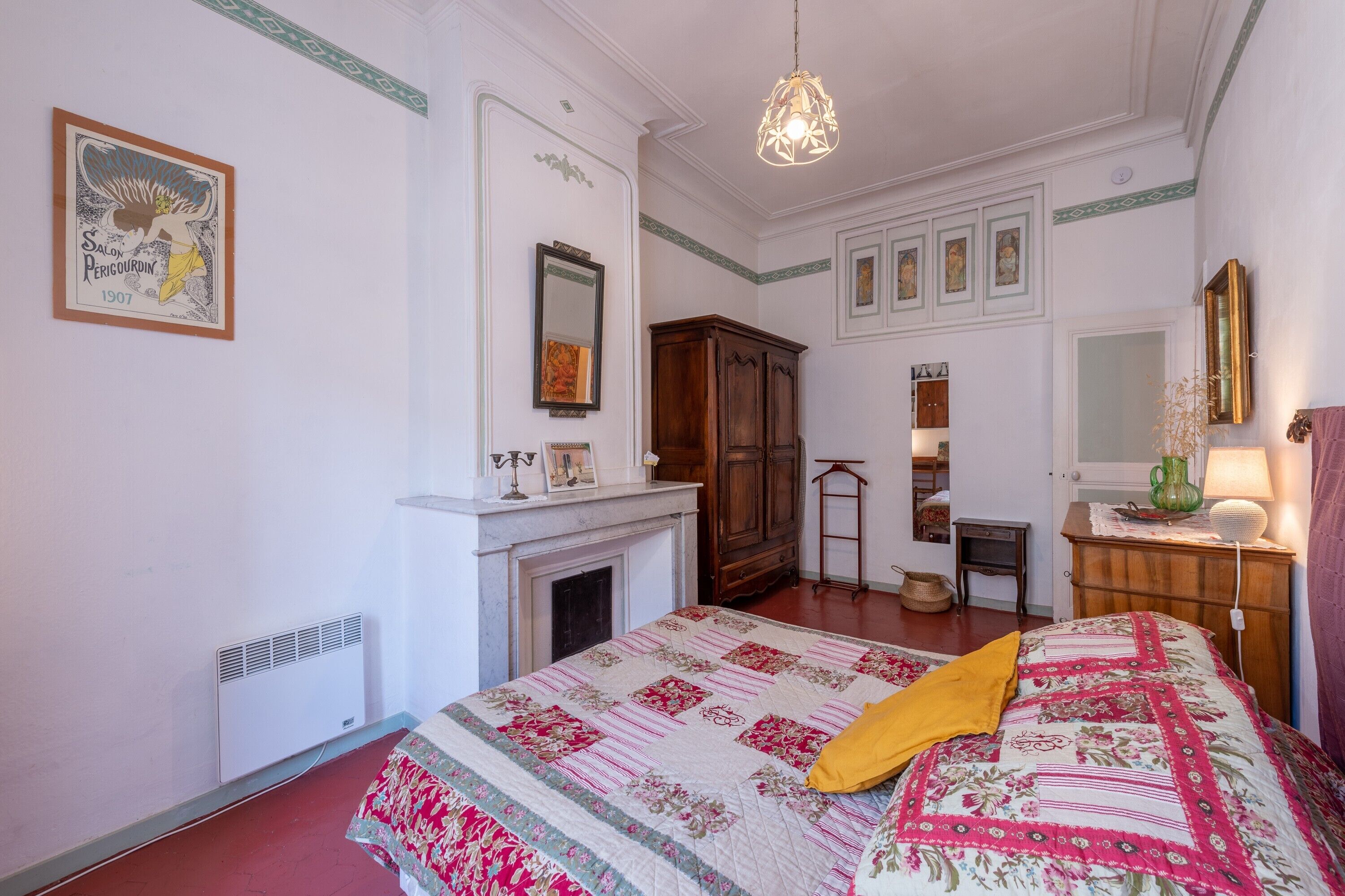 A bedroom with a bed, a fireplace, a wardrobe, a mirror, and a hanging light fixture.