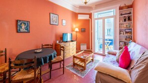 Un salon comprenant un canapé, une table à manger avec des chaises, un téléviseur et une bibliothèque.