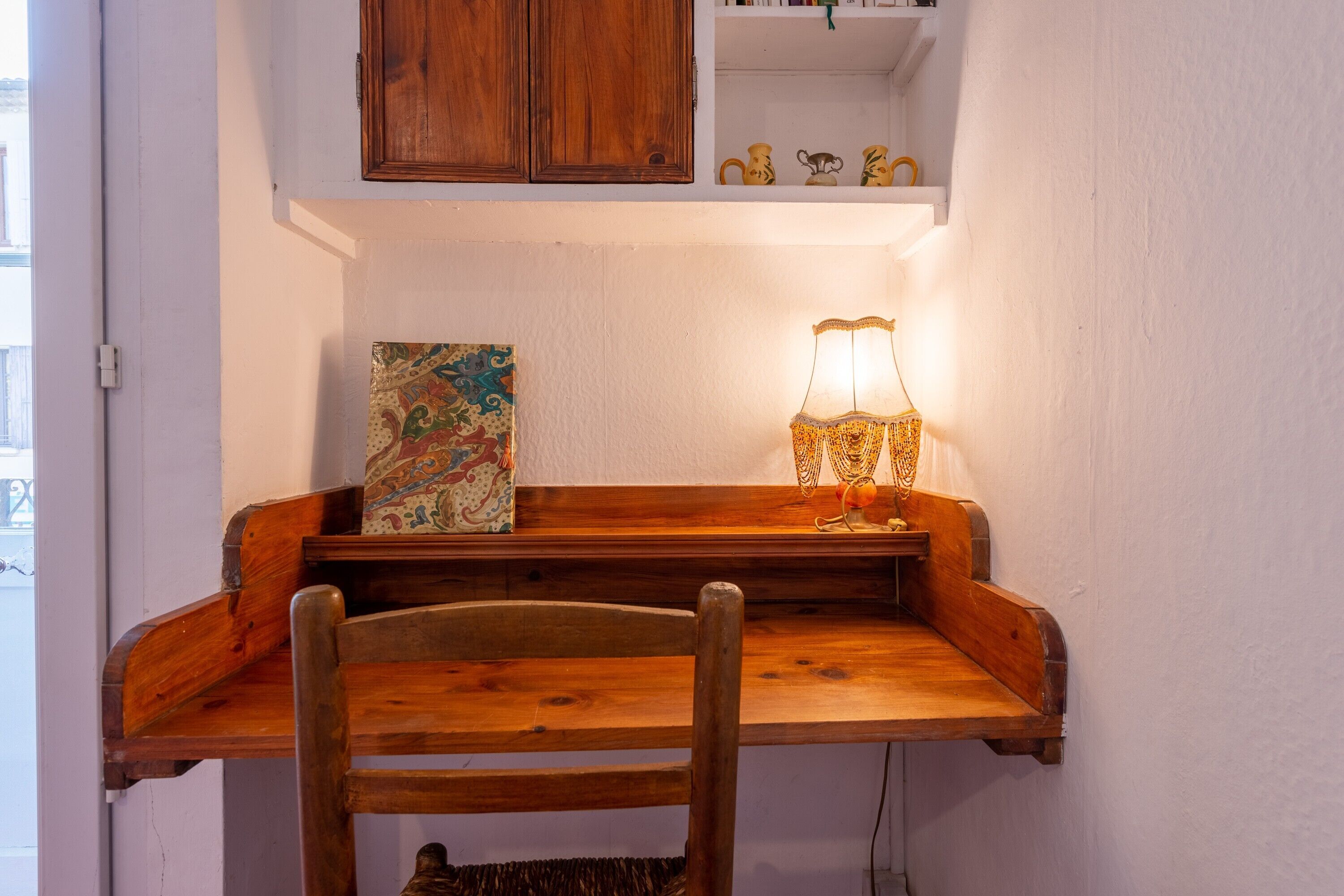 Una scrivania in legno con una lampada, una sedia e uno scaffale con oggetti decorativi.