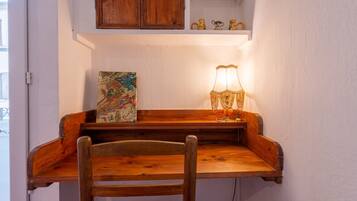 Una scrivania in legno con una lampada, una sedia e uno scaffale con oggetti decorativi.