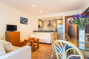 A living room with a sofa, TV, wooden cabinet, dining table, chairs, and a kitchen in the background.