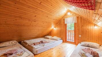 Una cabaña acogedora con paredes de madera y techo inclinado, que cuenta con dos camas con almohadas y mantas, un ventanal pequeño y una cortina roja a cuadros.