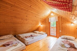 A cozy cabin with wooden walls and a sloped ceiling, featuring two beds with pillows and blankets, a small window, and a red checkered curtain. - Rudnica Hill Lodge With Private Garden (Podcetrtek)