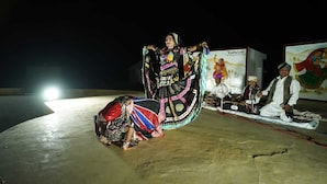 A person in traditional attire performing on a stage with a backdrop of a painting. - Kotri Resort (Jaisalmer)