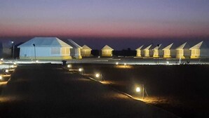 A series of dome-shaped buildings with a flat roof, illuminated by artificial lighting, set against a twilight sky. - Kotri Resort (Jaisalmer)