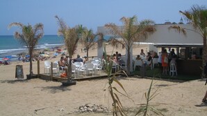 A beachside restaurant with outdoor seating, palm trees, and a view of the ocean. - Confort Apartamento con Excelentes Vistas al mar (VC)