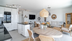 A modern kitchen with white cabinets, a dining area with a wooden table and wicker chairs, and a living area with a sofa and decorative items. - Villa Luxuria Private Pool by Casasol (Nerja)