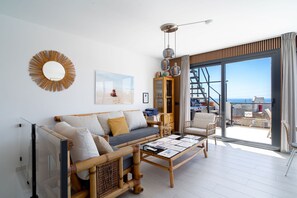 Una sala moderna con un sofá, sillones, una mesita de centro, un espejo grande y vistas al mar a través de un ventanal corredero.
