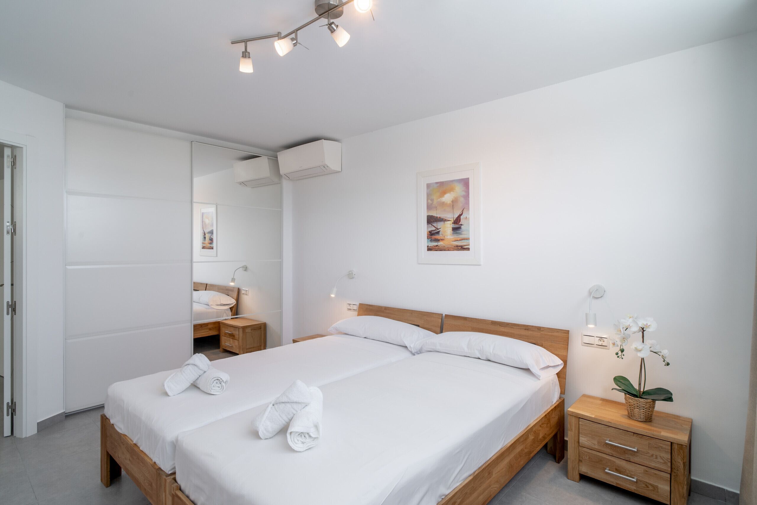 A modern hotel room with a large bed, bedside tables, a mirror, and a wall-mounted air conditioner.