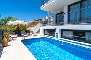 A modern pool area with a clear blue pool, sun loungers, and a glass balustrade overlooking a hillside. - Villa Luxuria Private Pool by Casasol (Nerja)