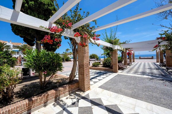 A covered outdoor area with a checkered floor, white pergola, and potted plants with flowers.
