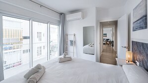Ein modernes Hotelzimmer mit einem großen Bett, einem Balkon, Blick auf die Stadt und einem Flur zum Essbereich.