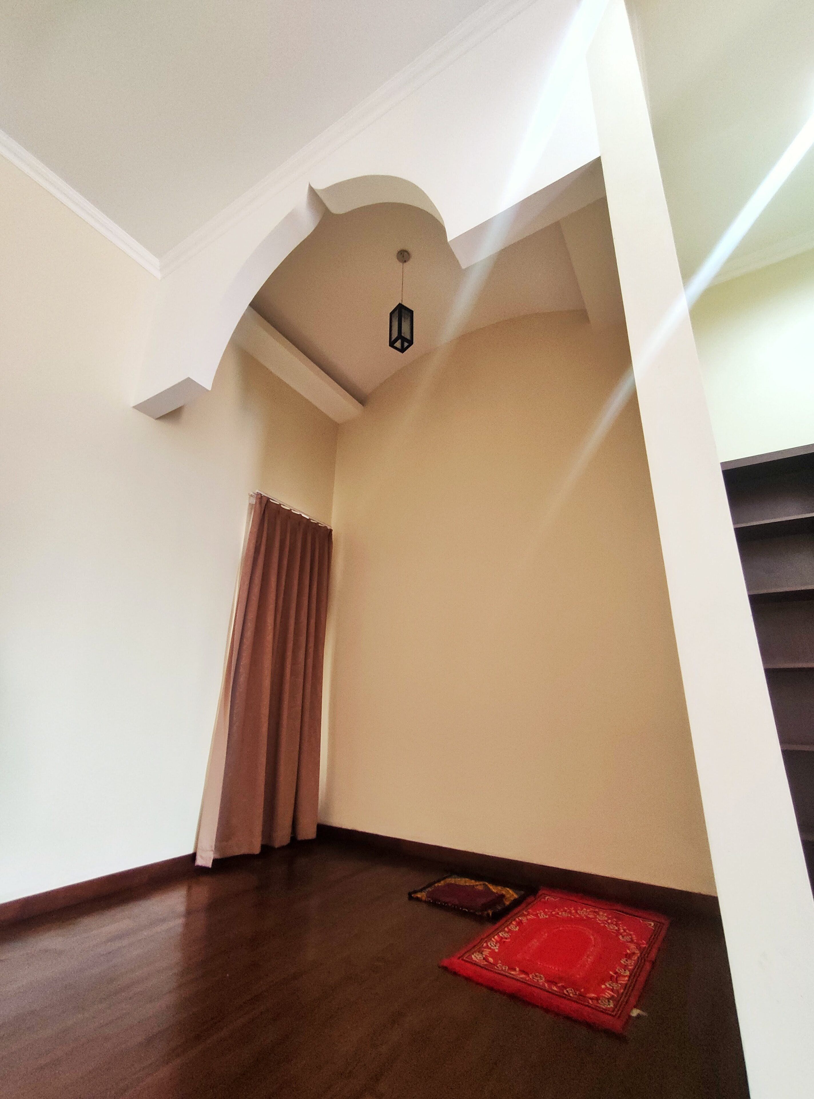 Um quarto com piso de madeira, tapete vermelho e luminária no teto.