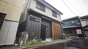 A two-story residential building with a modern facade, a wooden slatted wall feature, and a small garden area with plants. - TokinoyadoNijo (Kyoto)