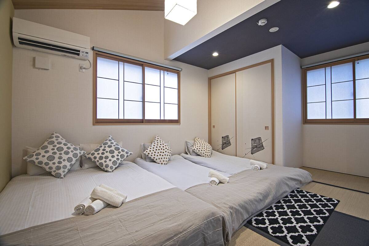 Habitación de hotel con dos camas, un ventanal grande, un equipo de aire acondicionado y una puerta corrediza tradicional japonesa.