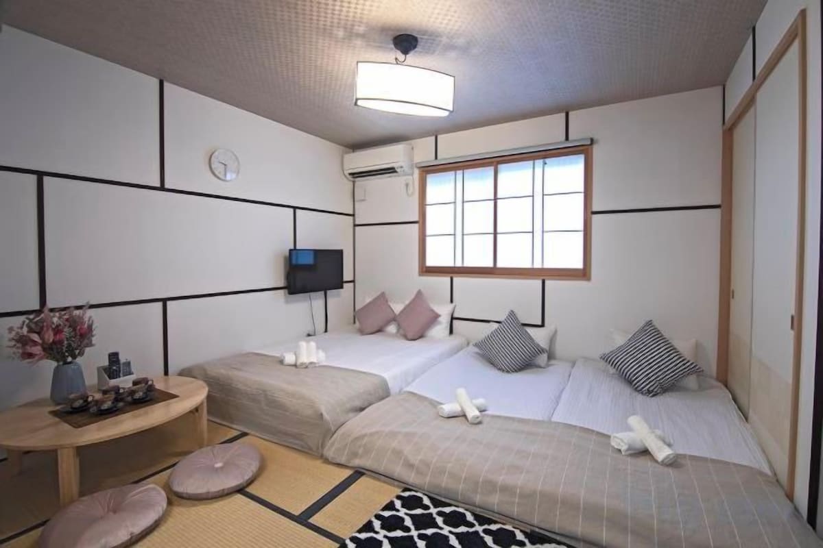 A hotel room with two beds, a TV, a small table, and a window.